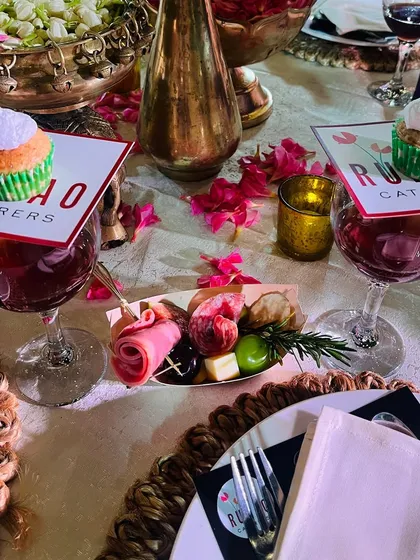 An intimate table setting featuring individual charcuterie boats with cured meats and cheese, alongside custom-branded cupcakes placed elegantly on wine glasses.