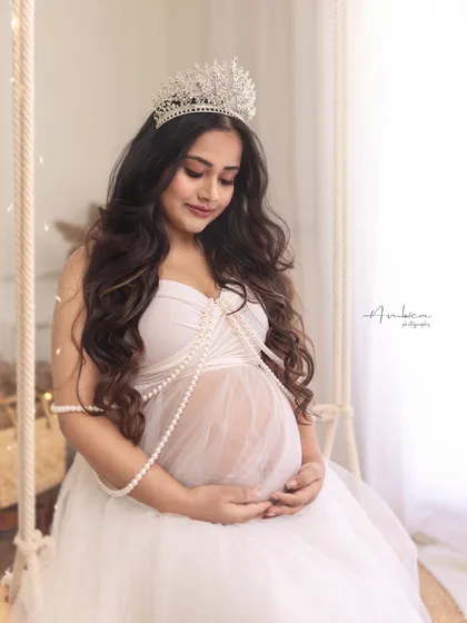 A quiet, contemplative moment on the swing. This shot focuses on the mother-to-be's connection with her baby, beautifully styled with a crown and pearls.