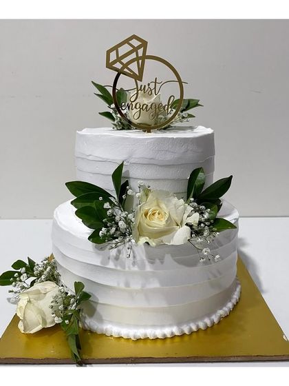 A pristine white two-tier engagement cake decorated with fresh white roses and baby's breath. This simple yet stunning design is perfect for a classic and elegant celebration.