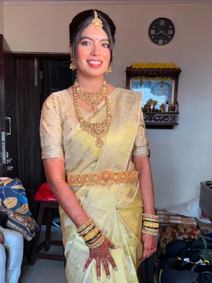 A full-length view of the bride in her elegant off-white and gold Kanjivaram saree, complete with a traditional waist belt (vaddanam).