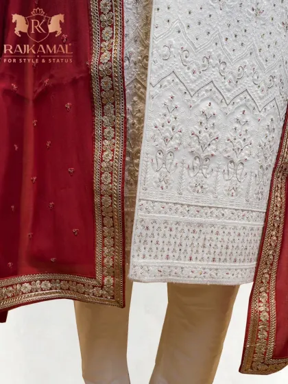 The rich texture of a red brocade stole, with its golden floral border, paired against the intricate embroidery of a white sherwani.