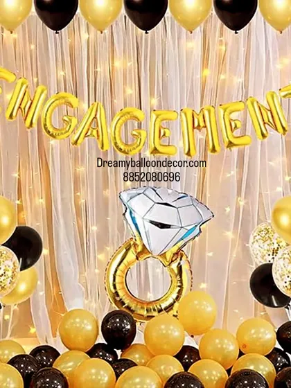 Celebrate your engagement with a stylish photo corner. This black and gold themed setup includes a 'Engagement' foil balloon banner, a giant ring prop, and a backdrop of fairy lights to capture the special moment.