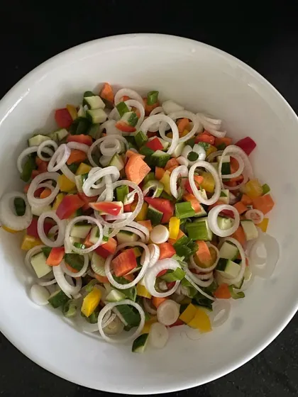 A bowl of freshly chopped vegetables ready for a salad. You can see the vibrant colors of bell peppers, carrots, cucumbers, and onions, all finely cut.