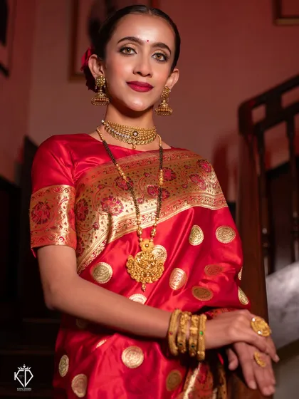 An indoor portrait using dramatic lighting to highlight the richness of the red saree and gold jewelry.