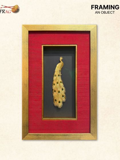 A single elegant peacock feather crafted in gold, framed as a singular statement. The simplicity of the object is enhanced by the opulent framing, proving that even smaller items can have a grand impact.