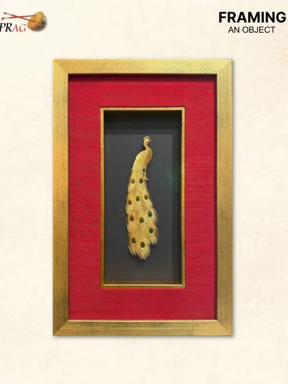 A single elegant peacock feather crafted in gold, framed as a singular statement. The simplicity of the object is enhanced by the opulent framing, proving that even smaller items can have a grand impact.