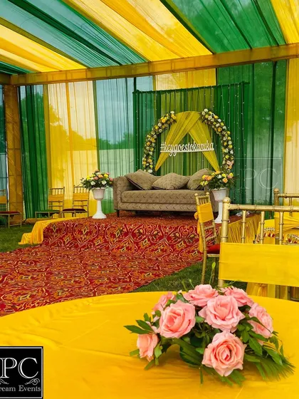 A wider view of the outdoor Mehndi setup, showing the tented area with green and yellow drapes and guest seating arrangements.