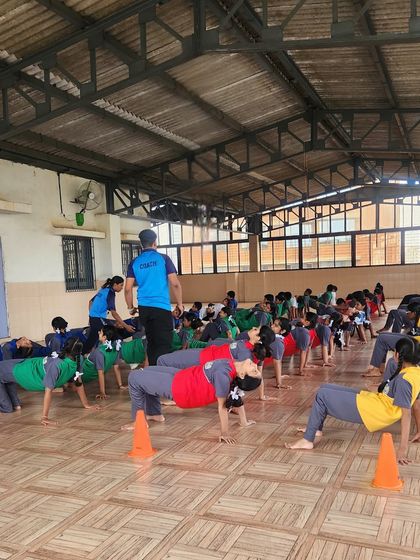 Students practice the reverse table-top pose during a large group yoga session. This pose helps build strength in the arms, legs, and core, demonstrating the physical benefits of yoga.