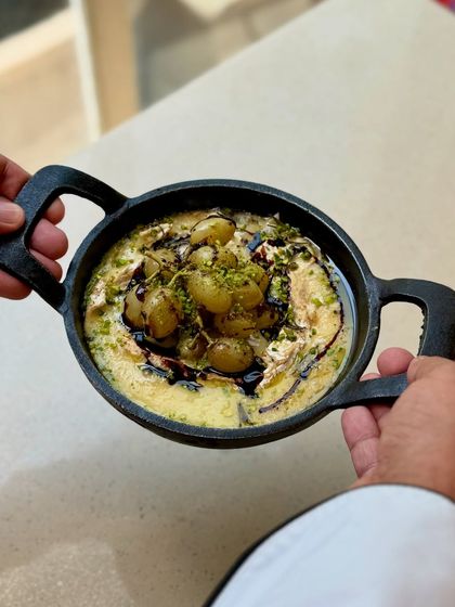 A top-down view of our oven-roasted Kumaoni grapes on melted brie. The dish is infused with farm-grown herbs, drizzled with balsamic, and sprinkled with pistachio dust.