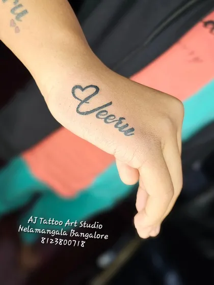 A simple "Veeru" name tattoo with a heart on the hand.