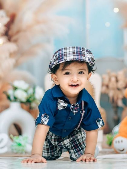 A dapper little gentleman crawling towards the camera during his first birthday studio session. The plaid outfit and teddy bear add a classic, charming touch.