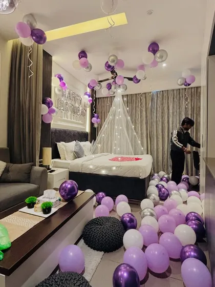 A beautiful room decoration in purple and silver tones, with balloons on the ceiling and floor, and a fairy light canopy over the bed.