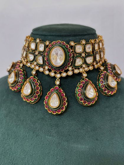 A close-up of a bridal choker with large Kundan stones and green and red Meenakari work. This is a classic rental choice.