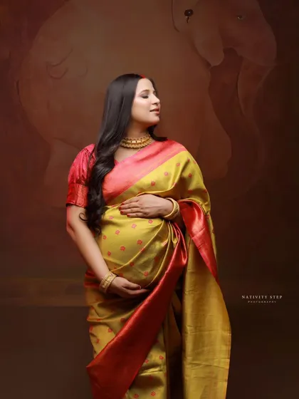 A profile shot of the mother-to-be cradling her bump. The rich fabric of the saree and the soft studio lighting create a timeless and elegant look.