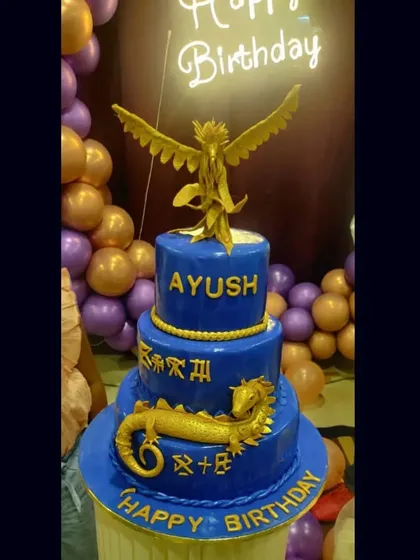 The final look of the stunning three-tiered Dragon and Phoenix cake, set against a festive party backdrop. The gold details on the royal blue fondant are truly striking.