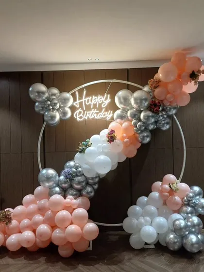 A slightly different angle of the peach and silver balloon ring, showing the 'Happy Birthday' neon sign.