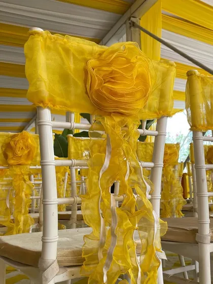 It's all in the details. A close-up of the chair decor for a Haldi ceremony, featuring a beautiful, large fabric flower tied with flowing yellow ribbons.