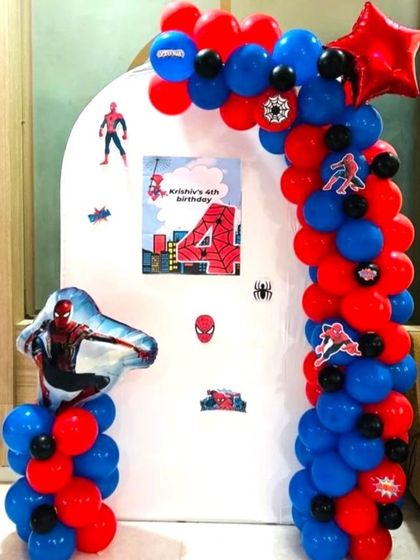 A simple Spiderman theme decoration for a 4th birthday at home. The setup includes a balloon arch and character stickers on a white arch backdrop.