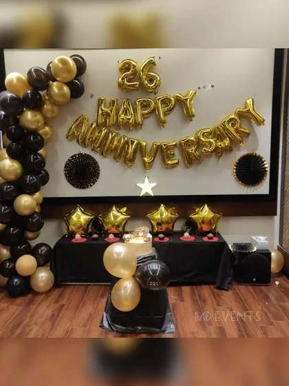 A classic and elegant 26th-anniversary decoration. This setup features a black and gold theme with a balloon garland and large 'Happy Anniversary' foil letters.