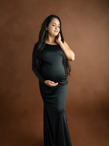 A simple yet stunning portrait of a mom-to-be in a black gown against a solid brown backdrop, emphasizing her form and serene expression.
