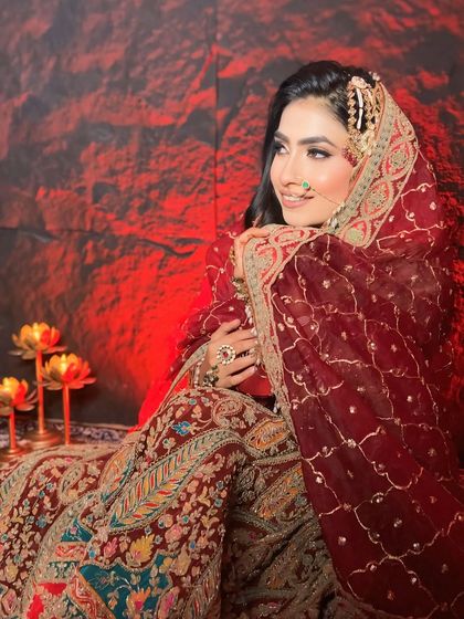 A candid shot of a bride in a traditional deep red lehenga. The soft, open hairstyle and glowing makeup create a timeless and beautiful bridal portrait.