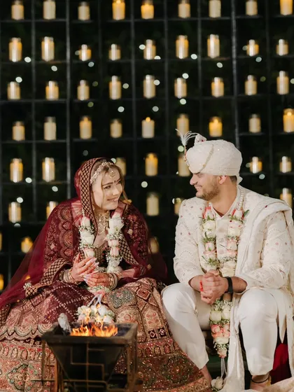 The couple shares a smile by the sacred fire, against a stunning backdrop of candles. This image captures the warmth and sanctity of the wedding rituals.