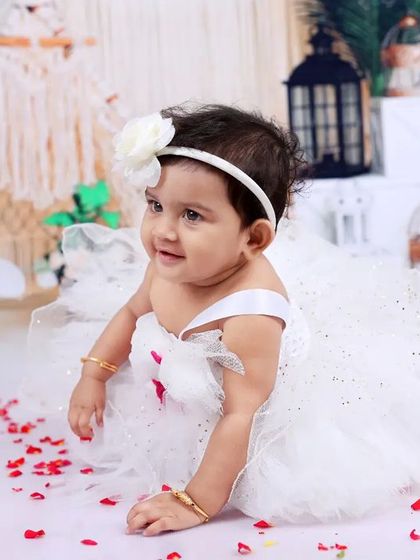 An elegant portrait of a baby girl in a white dress, sitting amidst a beautiful boho setup. The soft lighting and delicate props create a timeless and classic feel.