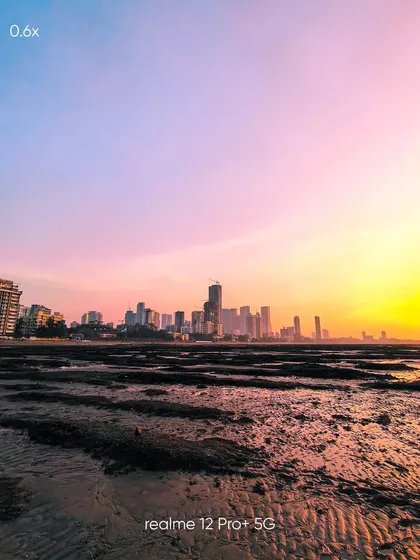 An ultra-wide 0.6x view of the Mumbai skyline at sunset. This mobile shot captures the vastness of the scene, from the foreground textures of the beach to the distant city lights.