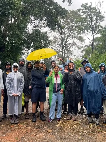 A group of trekkers waves and smiles on a rainy day, their spirits high. It's not just about the destination, it's about who you go with.