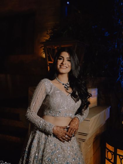 A beautiful evening portrait of a bride in her shimmering silver lehenga. The soft lighting highlights her smile and the sparkle of her outfit.