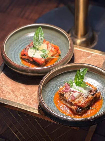 Two bowls of our sublime Eggplant Parmigiana, ready to be served. The rustic ceramic bowls complement the hearty, traditional nature of the dish.