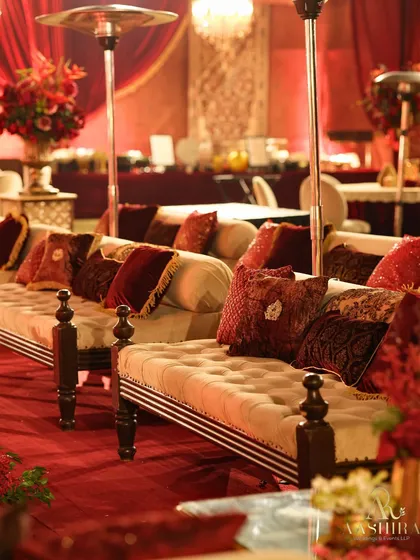Elegant diwan-style seating with plush tufted cushions in shades of red and maroon, providing a luxurious and comfortable space for guests to relax.