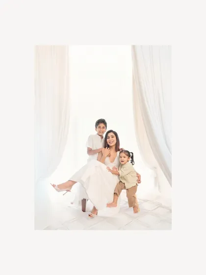 A mother sits gracefully with her two children in a bright, white studio setting. The image captures the love and gentle chaos of life with little ones, creating a beautiful and modern family portrait.
