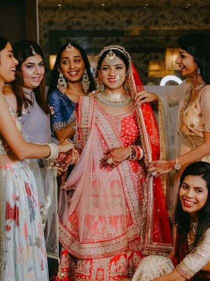 A beautiful moment between the bride and her bridesmaids. Her royal look features a red and pink lehenga with intricate jewelry.