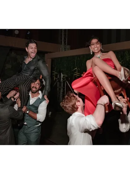Saumya and Sid get lifted onto chairs at their after-party, a classic celebration moment. Their expressions of pure joy and the energy of their friends make this a fantastic party shot.