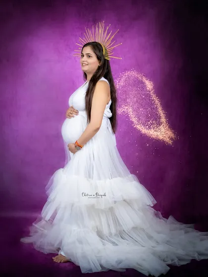An ethereal angel in white against a purple backdrop. The golden halo and sparkling wings add a magical touch to this maternity portrait.