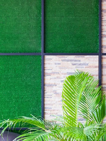 A custom vertical garden design featuring panels of artificial turf set within a sleek black metal frame against a textured stone wall. This image highlights how I combine different materials to create unique and stylish accent walls for both indoor and outdoor spaces.