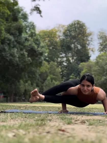 Holding an eight-angle pose (Astavakrasana) in a park. This arm balance requires a combination of core strength, hip flexibility, and a bit of playfulness.