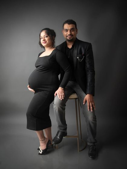 A classic and elegant studio portrait of an expecting couple. Dressed in black against a simple grey background, their connection and excitement are the main focus.
