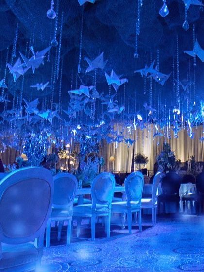 A wide view of the winter wonderland dining area. The entire ceiling is a canopy of blue netting, from which hang hundreds of paper origami birds and crystal strings, all bathed in a cool blue light.
