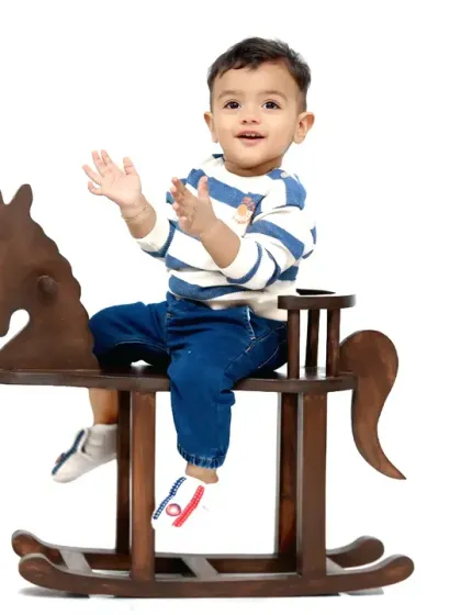 A happy toddler claps his hands while enjoying a ride on a classic wooden rocking horse against a clean white background.