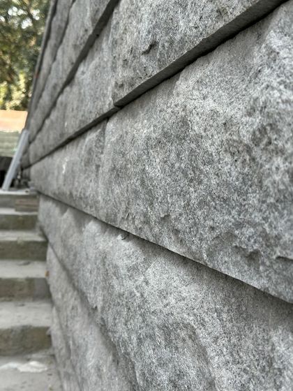 A close-up perspective of a stone wall under construction. The image highlights the geological character and solidity of the material.