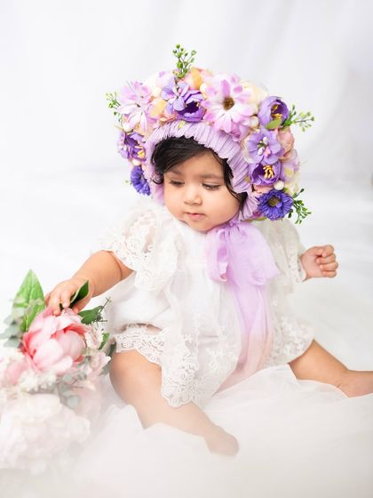 An eight-month-old baby curiously touches a bouquet of peonies during her floral-themed milestone photoshoot.