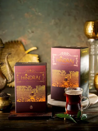 A dark and moody shot of Hindraj black tea packaging. The dramatic lighting highlights the intricate gold foil on the box, giving the product a mysterious and luxurious appeal.