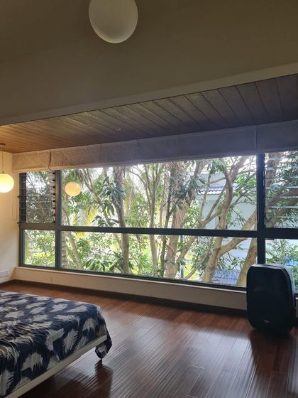 In this bedroom, the main feature is the expansive window offering a stunning view of a large mango tree. The design prioritizes the connection with nature, using a simple layout and wooden flooring to complement the outdoor scenery.