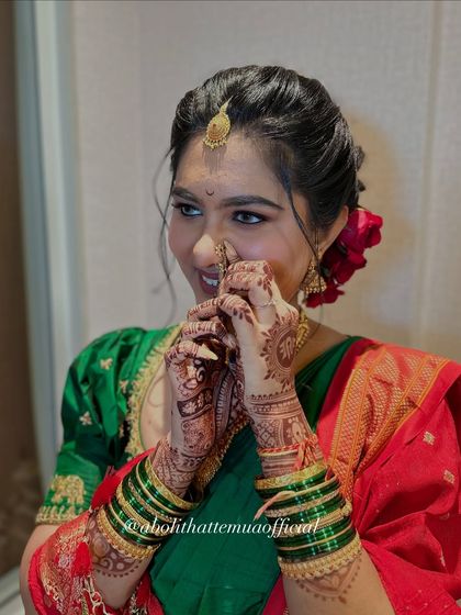 A playful moment captured as the bride adjusts her nath. This highlights the intricate henna design and the traditional green bangles, all part of the complete bridal look.