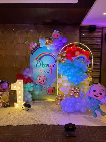 This is a duplicate of ID 1, 68, 137, 184, 190, 213, 226, 250. A vibrant Cocomelon theme for a first birthday party. This setup includes a custom arched backdrop, a rainbow-colored balloon arrangement, and a life-sized cutout of the character JJ.