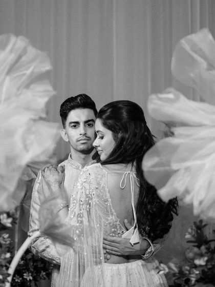 A black and white version of the couple's portrait. The dramatic lighting and the texture of the giant paper flowers create a timeless and artistic image.