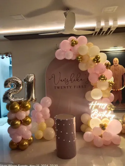 A beautiful 21st birthday setup in pastel pink and gold, featuring a custom backdrop, balloon arch, and a neon "Happy Birthday" sign.
