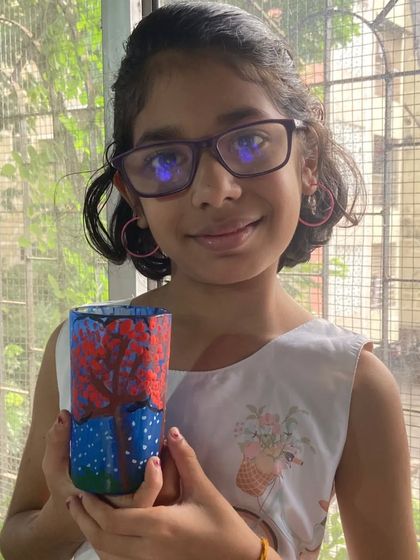 Spruha, a 4th standard student, shows off her glass painting. She has painted a beautiful seasonal tree on a glass, learning how to use special paints for a transparent effect.